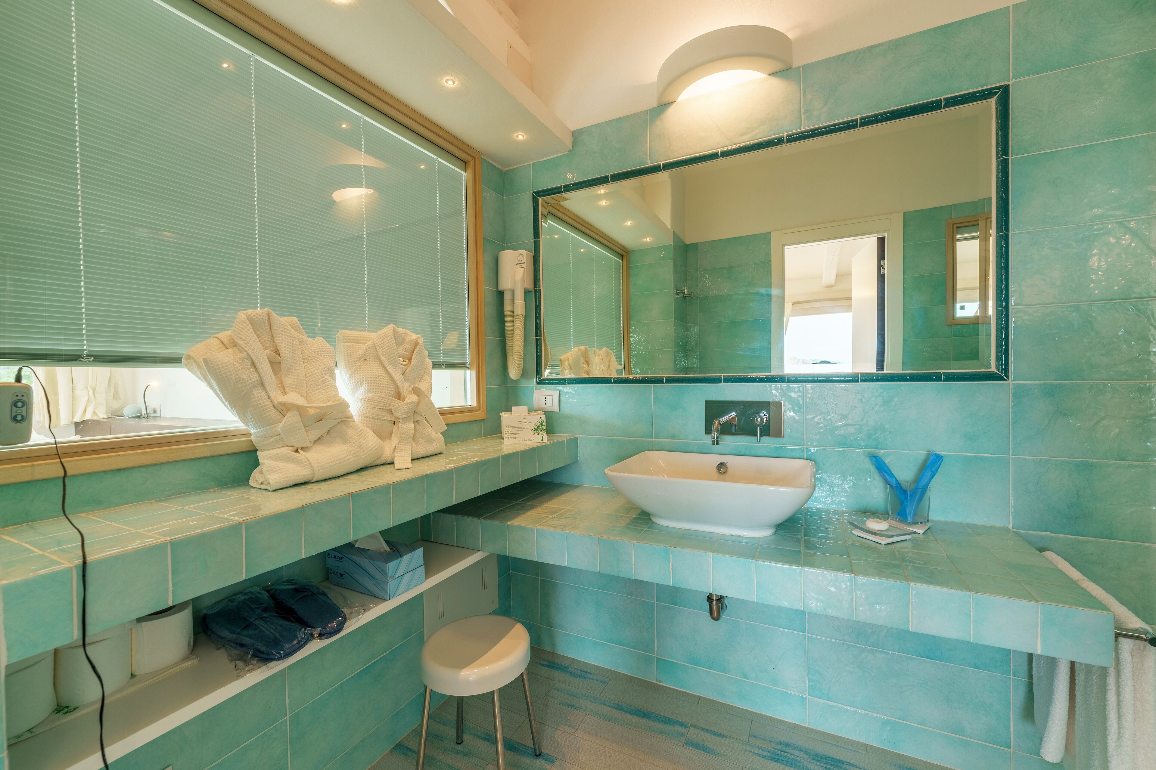 Un baño con un espejo grande, un lavamanos y una ventana con persianas.