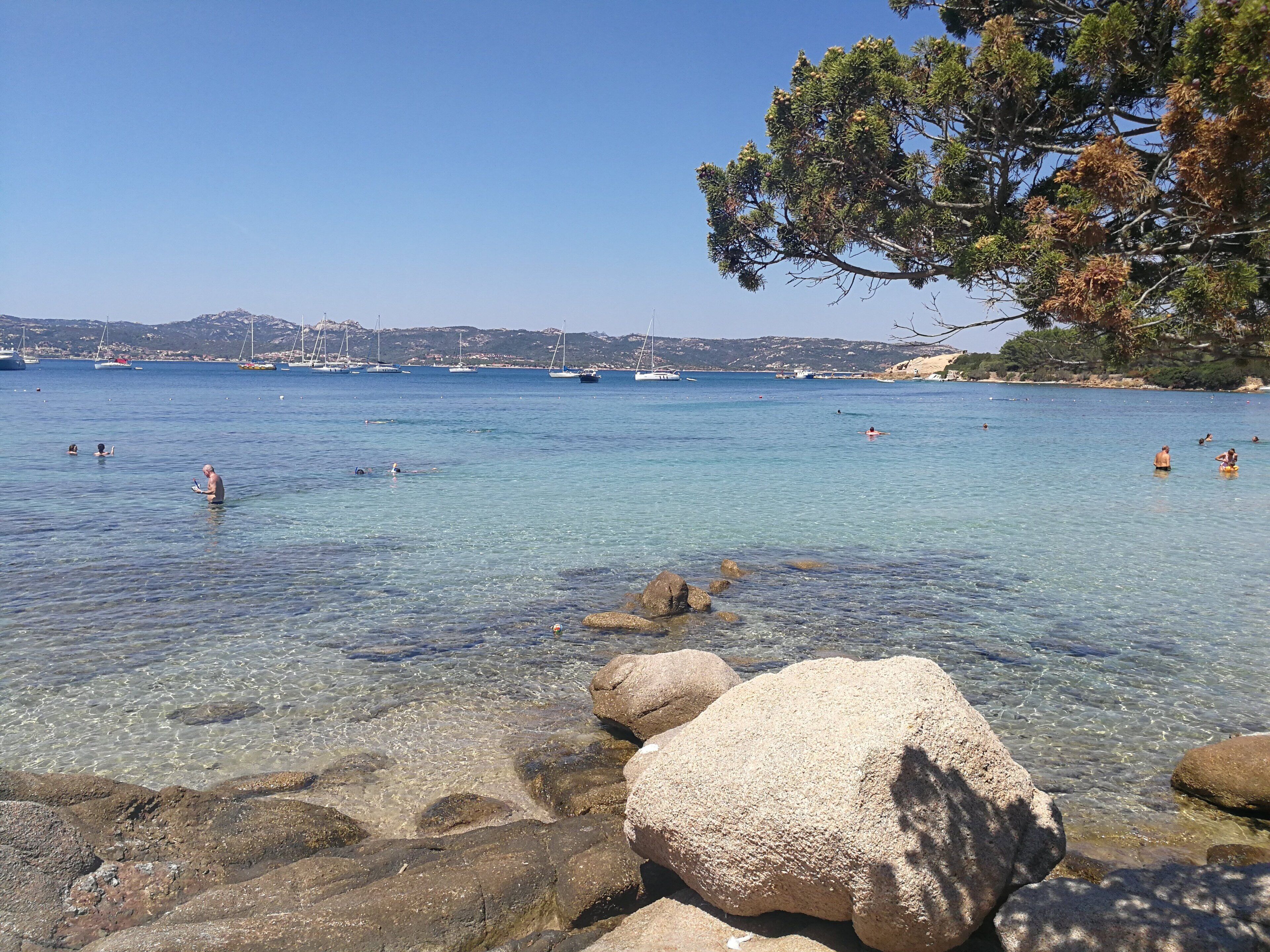 A clear coastal area with rocky shores and boats in the background.