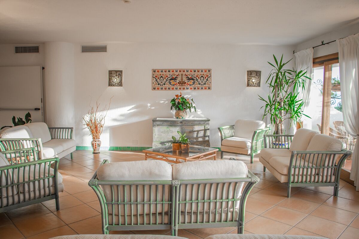 Un salón amplio con mobiliario de mimbre, una mesa de centro y plantas decorativas.