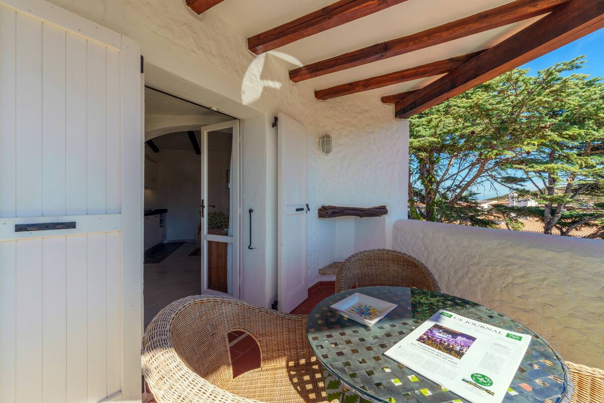 An outdoor patio with wicker furniture, a glass table, and a door leading to an interior space.