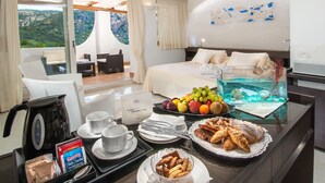 Ein Hotelzimmer mit Bett, einem Esstisch mit Frühstücksangeboten, einer Kaffeemaschine und Blick ins Freie.