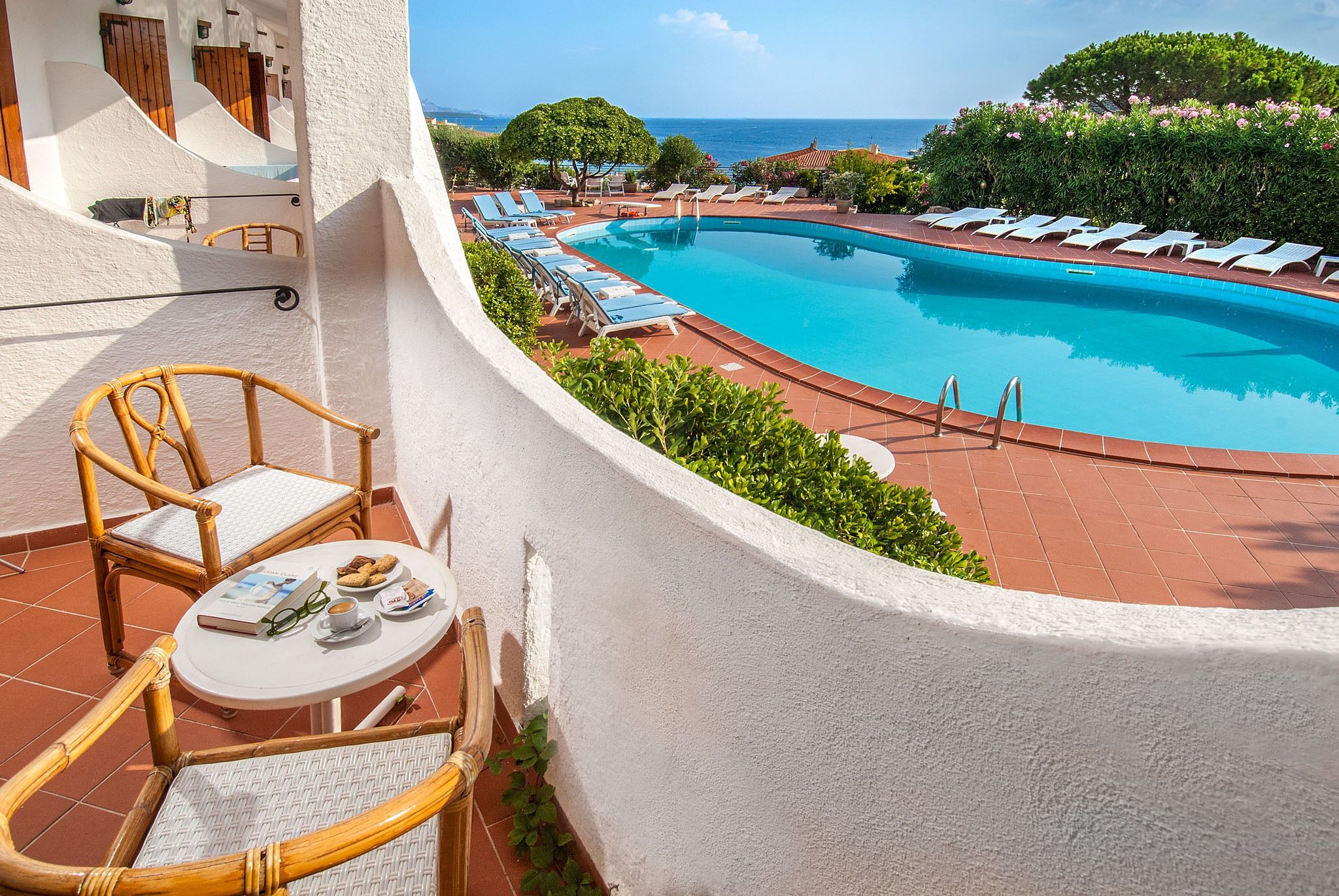 A poolside area with lounge chairs, a table with a book and glasses, and a view of the sea.