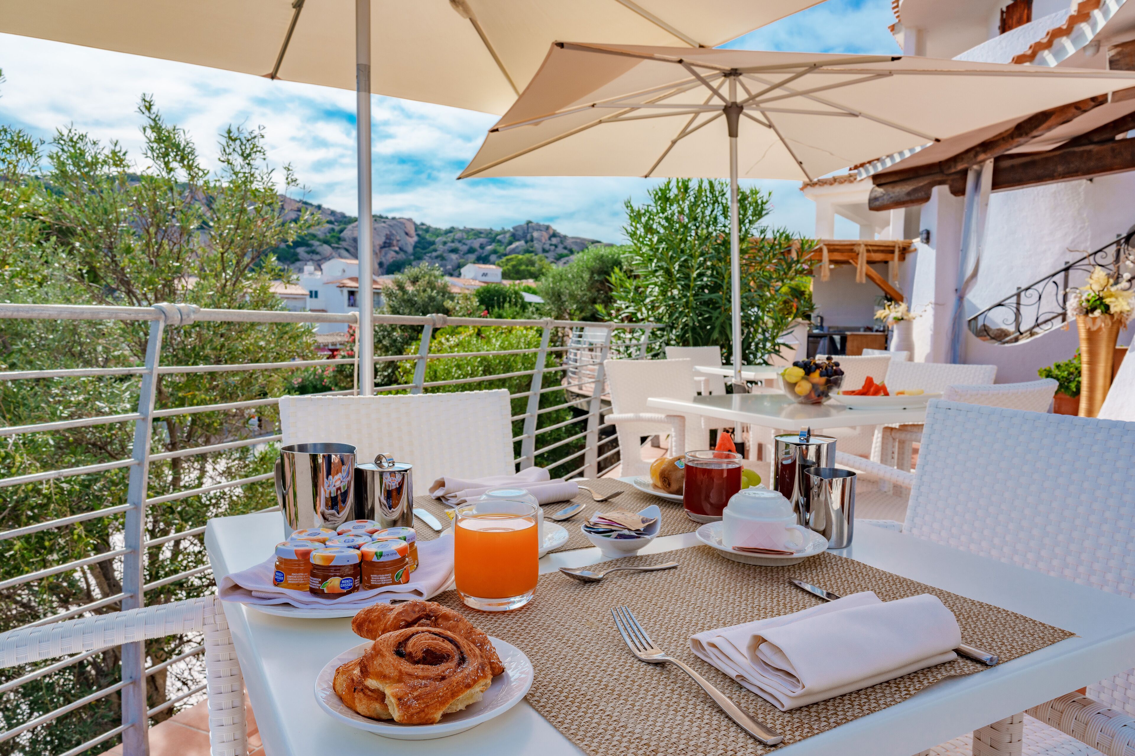 An outdoor dining area with a table set for breakfast, including pastries, juice, and condiments.