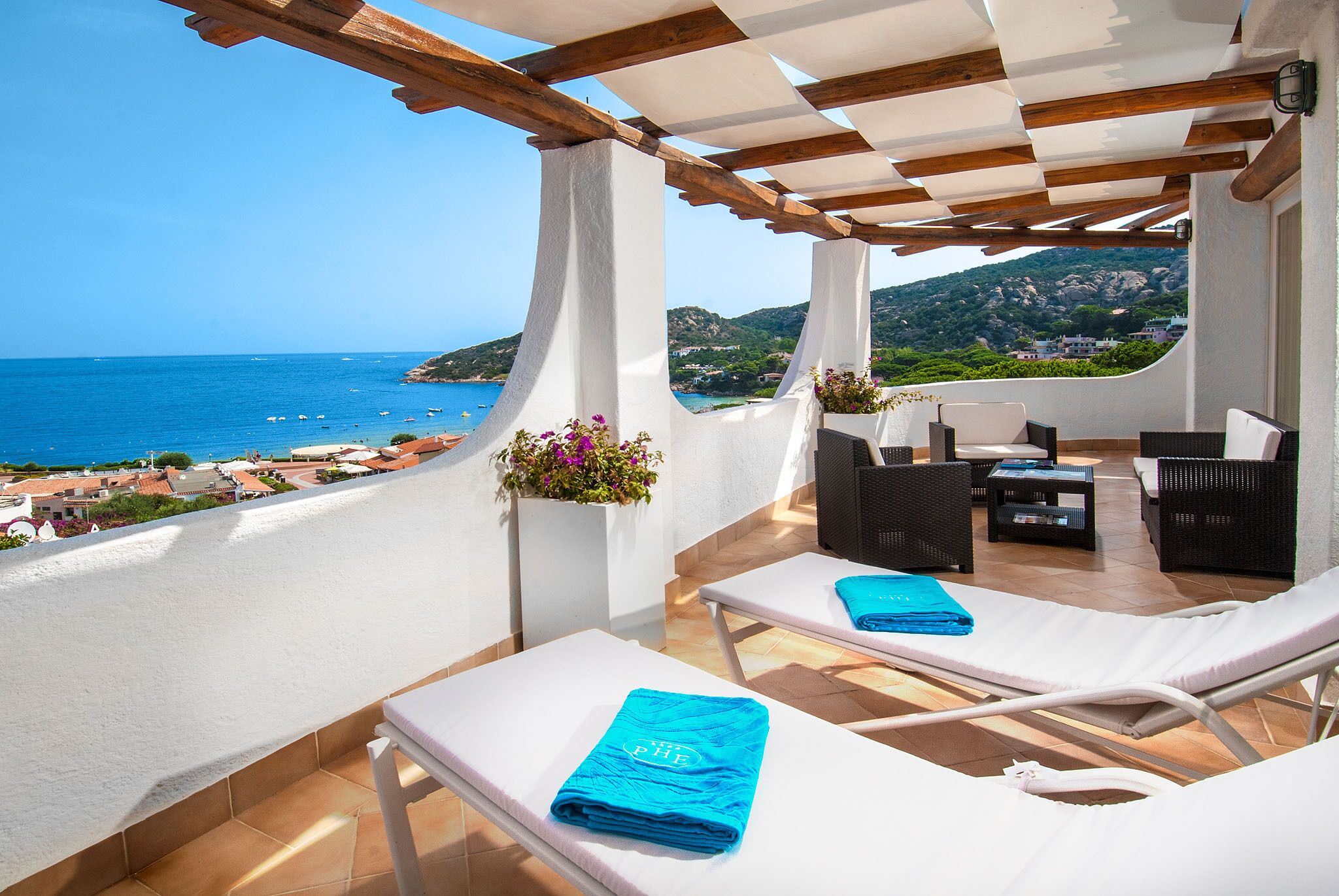 Eine Terrasse mit weißen Liegestühlen, einer Holzpergola und Blick auf das Meer und die Hügel.