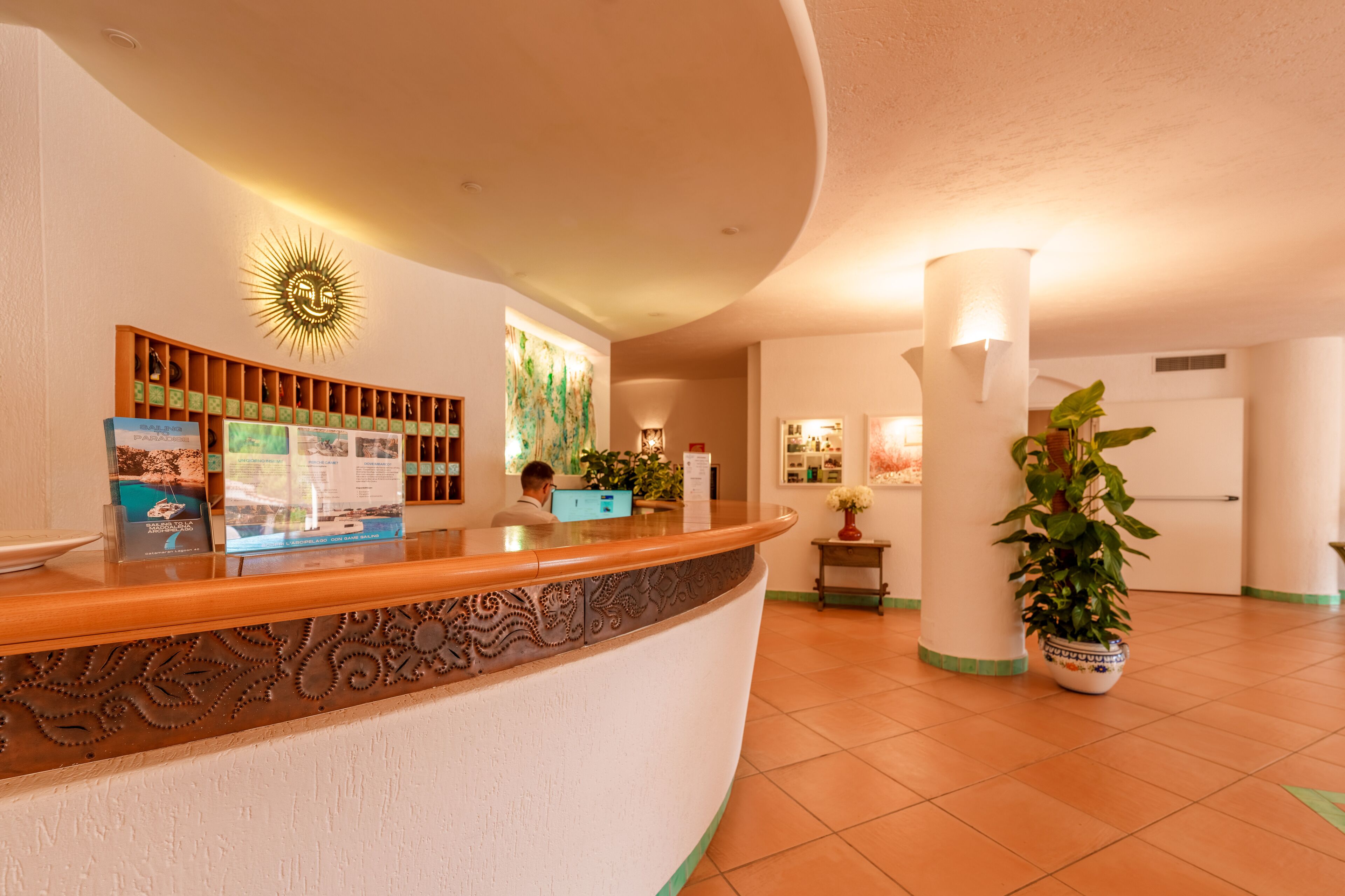 Zona de recepción de un hotel con un mostrador de madera curvo, una decoración en forma de sol y un escritorio de recepción.
