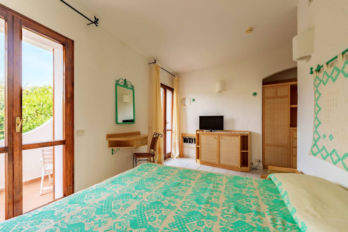 A bedroom with a bed, a TV, a wooden cabinet, a chair, and a window.