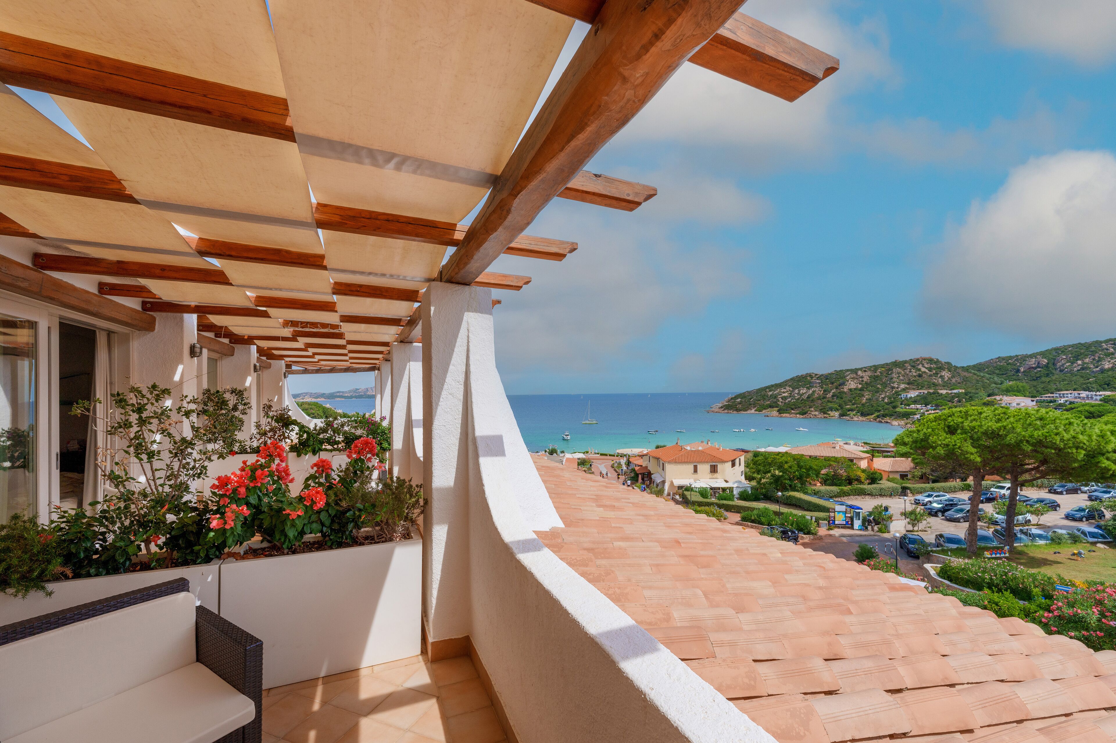 A balcony with a view of the sea, a tiled floor, and a wooden pergola.