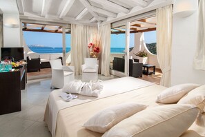 A modern hotel room with a large bed, a TV, and a balcony with a view of the sea. - Hotel Punta Est (Arzachena)