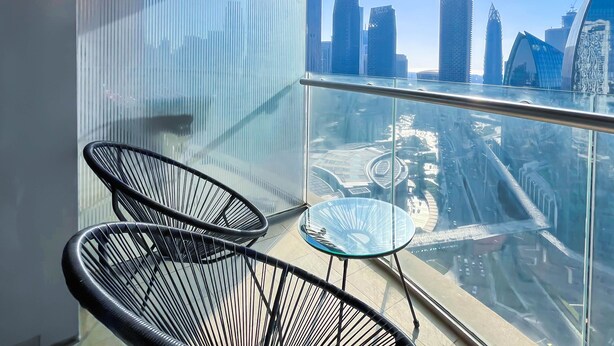 A balcony with a glass railing, two black wire-framed chairs, a small glass table, and a cityscape view. - Luxury residence at Fashion Avenue Dubai Mall (Dubai)
