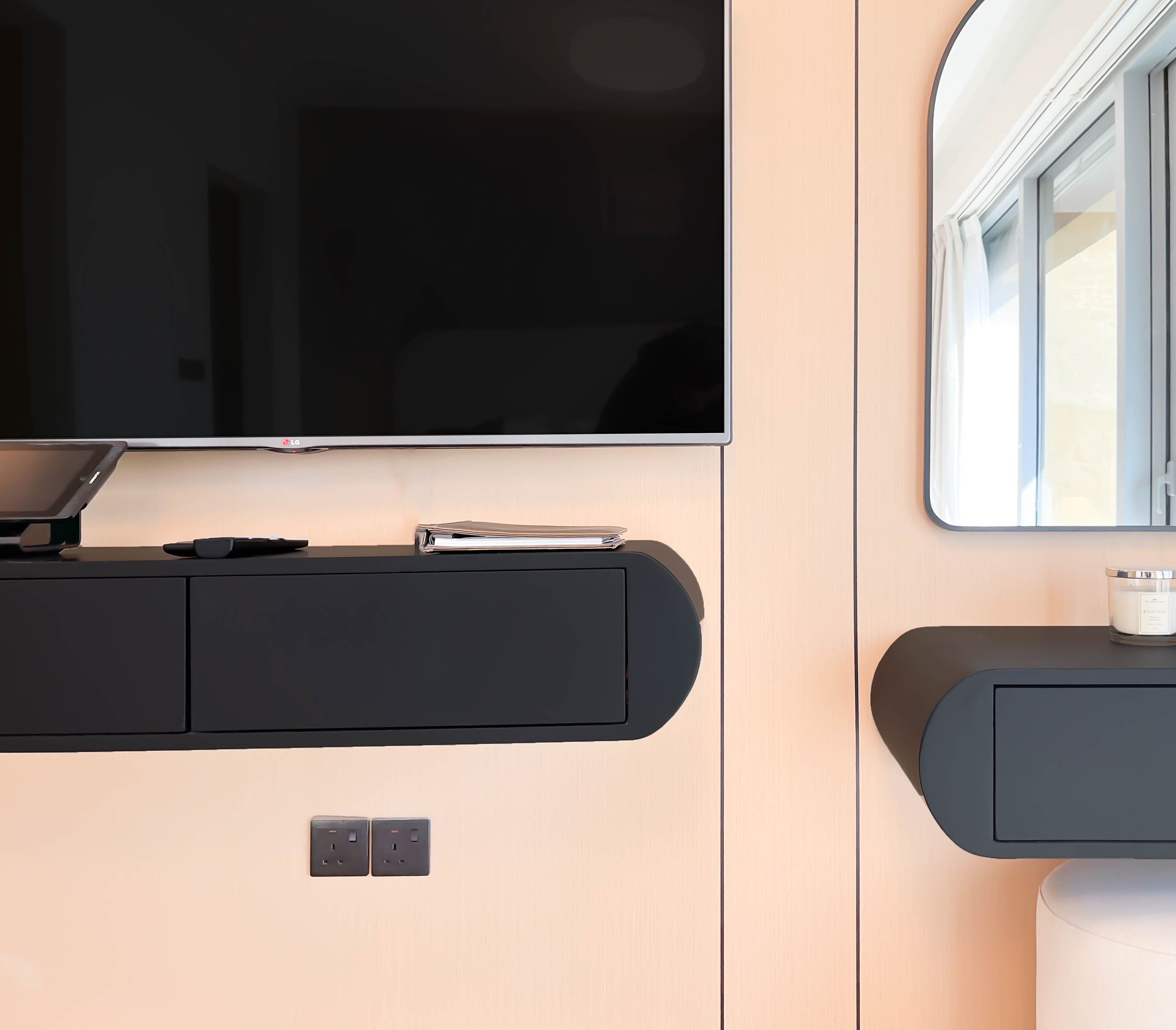 Un intérieur moderne avec un téléviseur à écran plat fixé au-dessus d’un meuble noir pour appareils multimédias, une petite table avec une bougie et une fenêtre avec des rideaux.