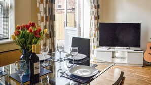 Un coin repas avec une table dressée pour deux personnes, un vase de tulipes et une bouteille de vin.