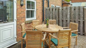 Une terrasse avec une table ronde et six chaises en bois, une bouteille de champagne et une clôture en bois en arrière-plan.