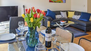 Un coin repas avec une table dressée pour deux personnes, un vase de tulipes, une bouteille de vin et un tableau accroché au mur.