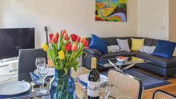 Ein Essbereich mit einem Tisch für zwei Personen, einer Tulpenvase, einer Weinflasche und einem Gemälde an der Wand.