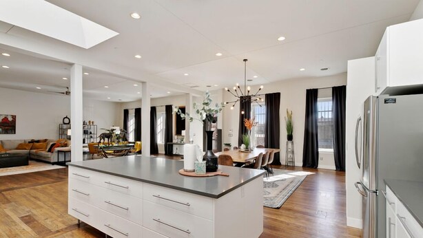 Una cocina moderna con una isla grande, armarios blancos y un refrigerador de acero inoxidable.