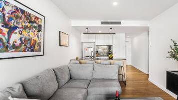 A modern living room with a grey sectional sofa, a wooden coffee table with a wine bottle and glass, and a colorful abstract painting on the wall.