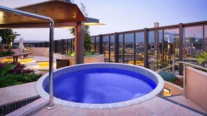 Ein Pool auf dem Dach mit Blick auf die Stadt, umgeben von Sitzgelegenheiten im Freien und einem überdachten Bereich.