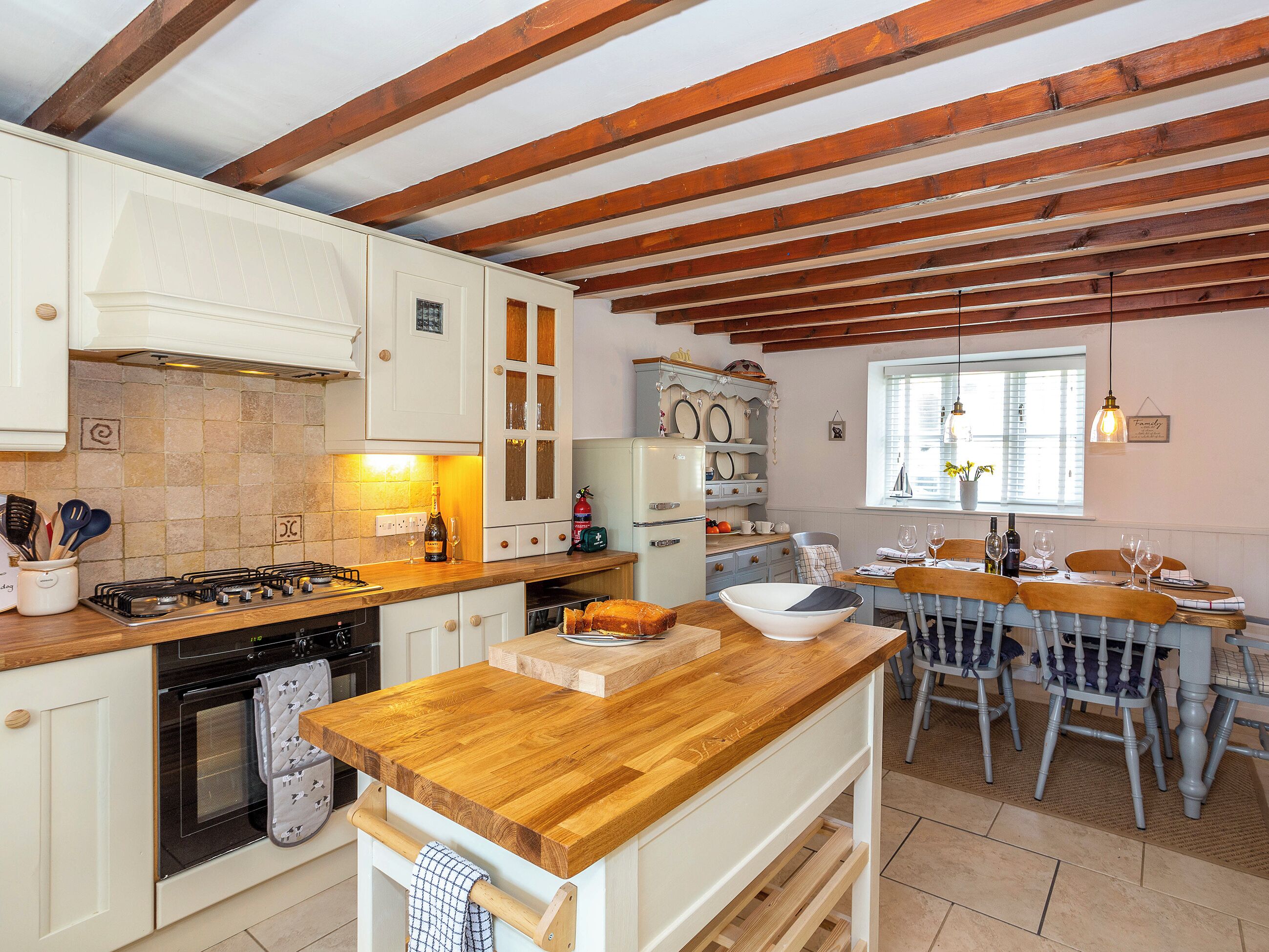 A kitchen with wooden beams, white cabinets, a wooden countertop, and a dining area with a table and chairs.