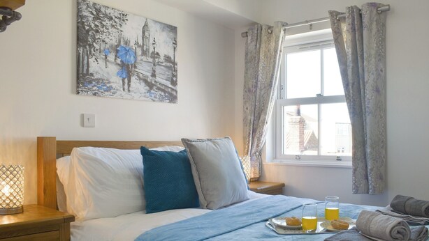 Ein ordentlich bezogenes Bett mit blauer Decke, Kissen und einem Tablett mit Orangensaft und einem Gebäckstück.