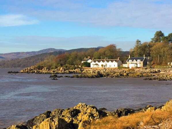 A coastal property with multiple white buildings, a rocky shoreline, and a backdrop of hills.