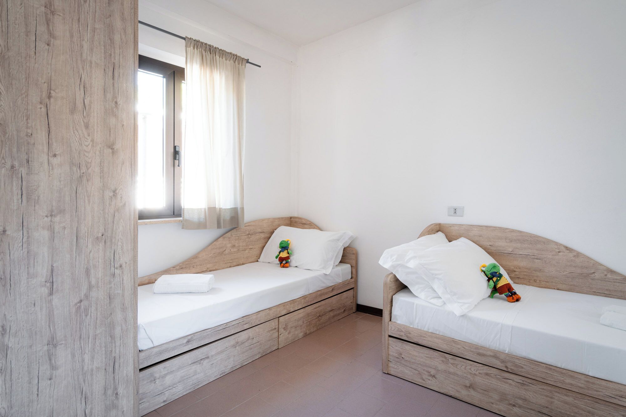 Two wooden bunk beds with white bedding and a window with curtains.