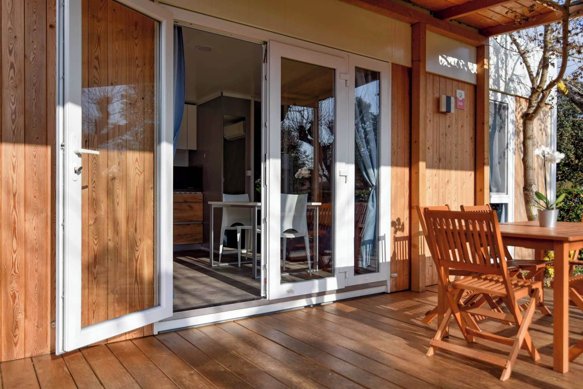 Una terraza de madera con una mesa y sillas, una puerta corrediza de vidrio que da a un espacio interior y un letrero con un número de habitación.