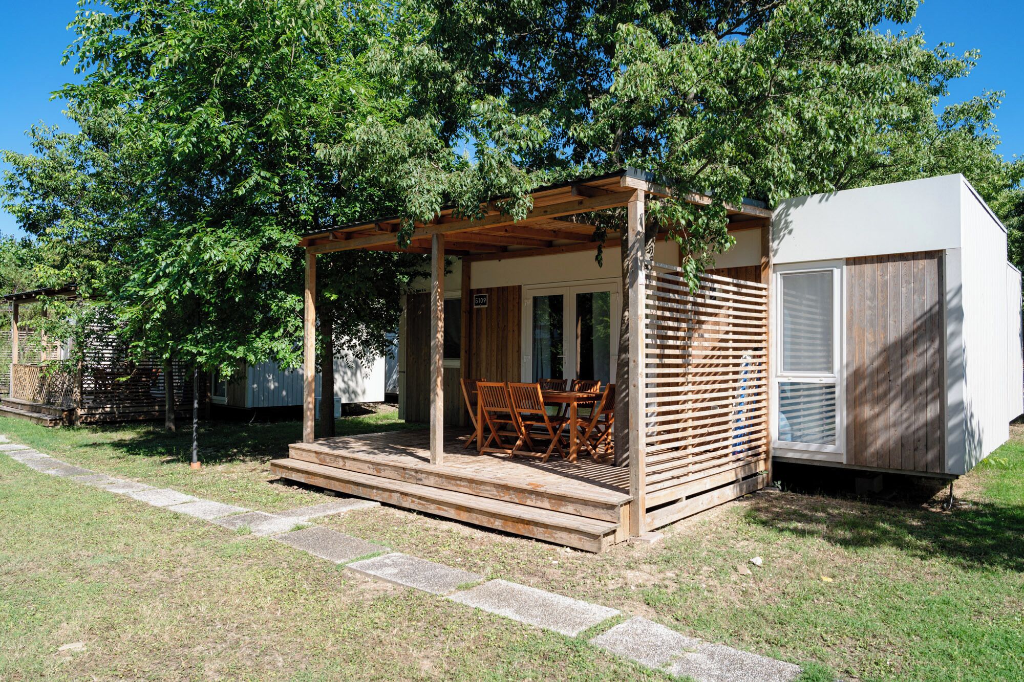 A wooden gazebo with a table and chairs, a white building with a window, and a fenced area.