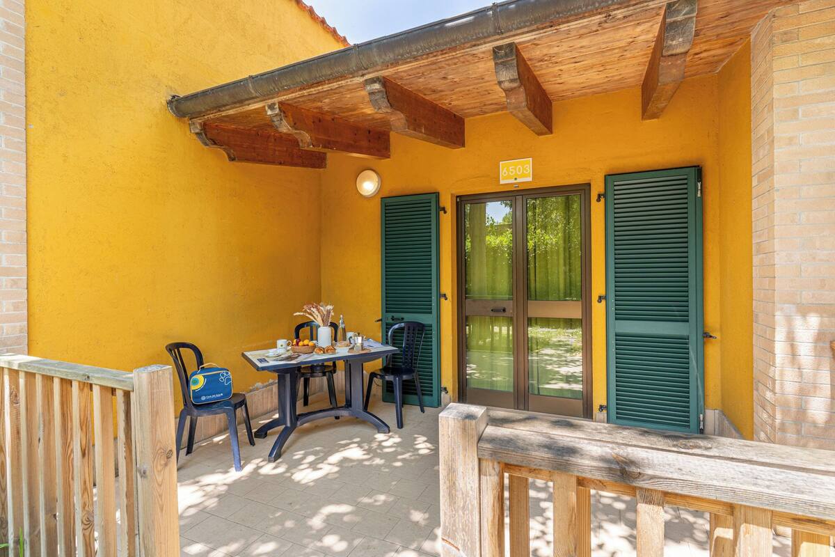A yellow building with a wooden ceiling, a table with chairs, and a door with shutters.