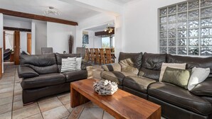 A spacious living room with two leather sofas, a wooden coffee table, and a large window with decorative glass panels. - Villa Suenios - PlusHolidays (Calpe)