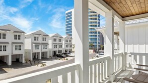 A beachfront hotel with multiple white buildings, a covered outdoor area with a wooden ceiling, and a view of a tall blue building in the background. - Beach Side Home, Steps from the Sand. Ocean Edge 05 | Bright Side by Kaiser Vacation Rentals. (Orange Beach)