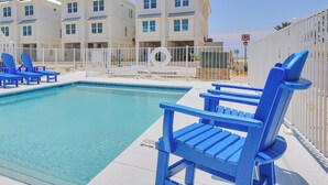 A swimming pool with blue chairs and a white building in the background. - Beach Side Home, Steps from the Sand. Ocean Edge 05 | Bright Side by Kaiser Vacation Rentals. (Orange Beach)