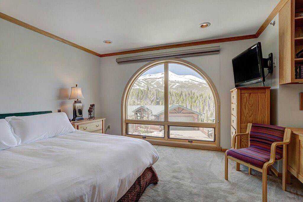 Une chambre avec une grande fenêtre, un lit, une chaise, un téléviseur et une armoire en bois.