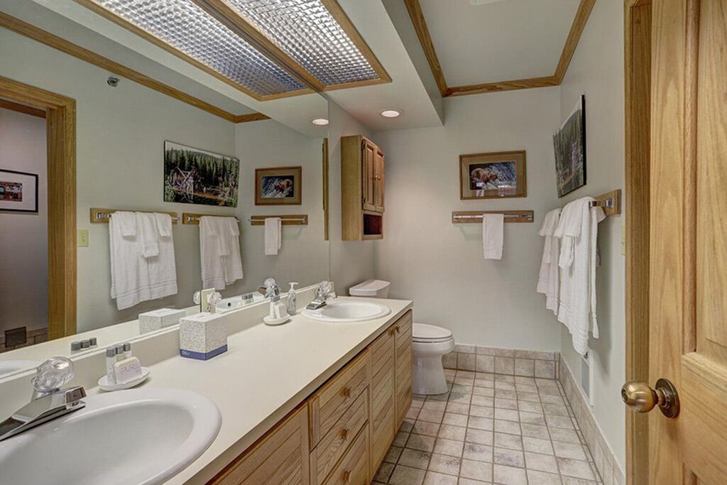 A bathroom with a large mirror, two sinks, a toilet, and wooden cabinets.