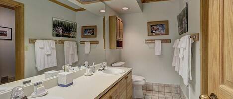 A bathroom with a large mirror, two sinks, a toilet, and wooden cabinets.