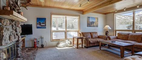 Una sala de estar acogedora con chimenea de piedra, sofás de cuero y un ventanal con vistas al exterior.
