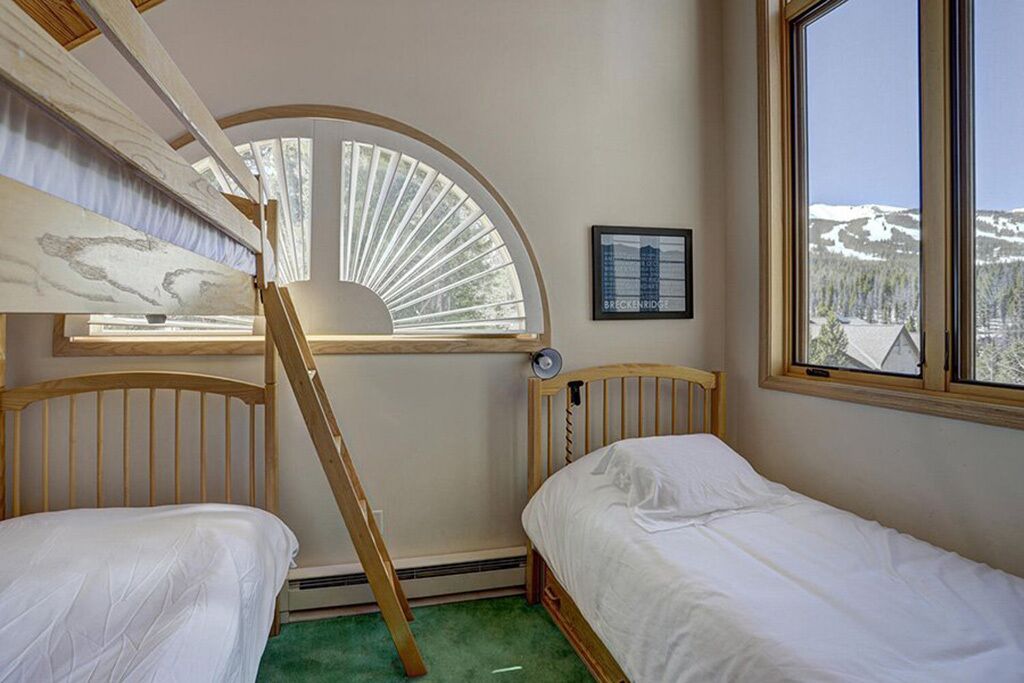 A room with two wooden bunk beds, a large window with a view of snow-capped mountains, and a framed picture on the wall.