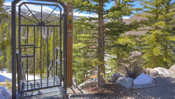 A metal gate with a wooden post, surrounded by trees and rocks, leading to a mountainous area. - Ski in/Ski Out 100 yards, Masive Views, On Shuttle Route, Hot Tub, Fireplace (Breckenridge)