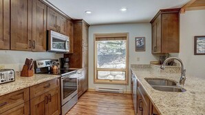 A kitchen with wooden cabinets, a microwave, a stove, a sink, and a window with a view of trees. - Ski in/Ski Out 100 yards, Masive Views, On Shuttle Route, Hot Tub, Fireplace (Breckenridge)