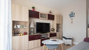 A modern living room with a flat-screen TV, wooden cabinets, a small round table, and a sofa. - LE VINTAGE - 300m plage - Wifi - Parking (Saint-Nazaire)