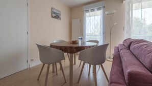 A dining area with a round table and two chairs, a purple sofa, and a window with sheer curtains. - LE VINTAGE - 300m plage - Wifi - Parking (Saint-Nazaire)
