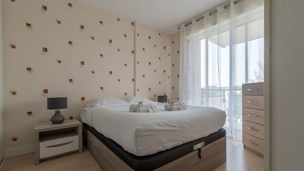A bedroom with a bed, nightstand, dresser, and large windows. - LE VINTAGE - 300m plage - Wifi - Parking (Saint-Nazaire)
