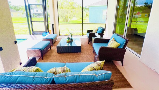 A sunlit patio with wicker furniture, large windows, and a view of a green lawn. - By Disney Universal Pvt. Pool Sleeps 10! Game rm Free Bbq, Parking,WiFi, Fishing (Kissimmee)
