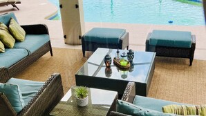 A covered outdoor seating area with wicker furniture and a glass coffee table, overlooking a swimming pool and a grassy lawn. - By Disney Universal Pvt. Pool Sleeps 10! Game rm Free Bbq, Parking,WiFi, Fishing (Kissimmee)