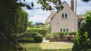 A quaint house with a well-maintained garden, a visible chimney, and a patio with outdoor furniture.
