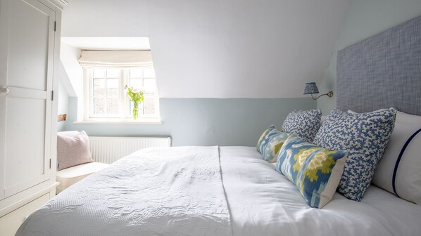 A bedroom with a bed, pillows, a window, and a radiator. - Thatch Cottage - sleeps 6 guests in 3 bedrooms (Todenham)
