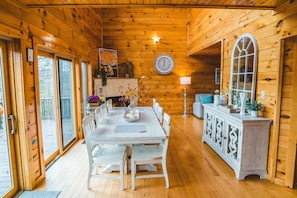 Ein Interieur einer Holzhütte mit Esstisch, Stühlen, einem Schrank und einem großen Fenster.