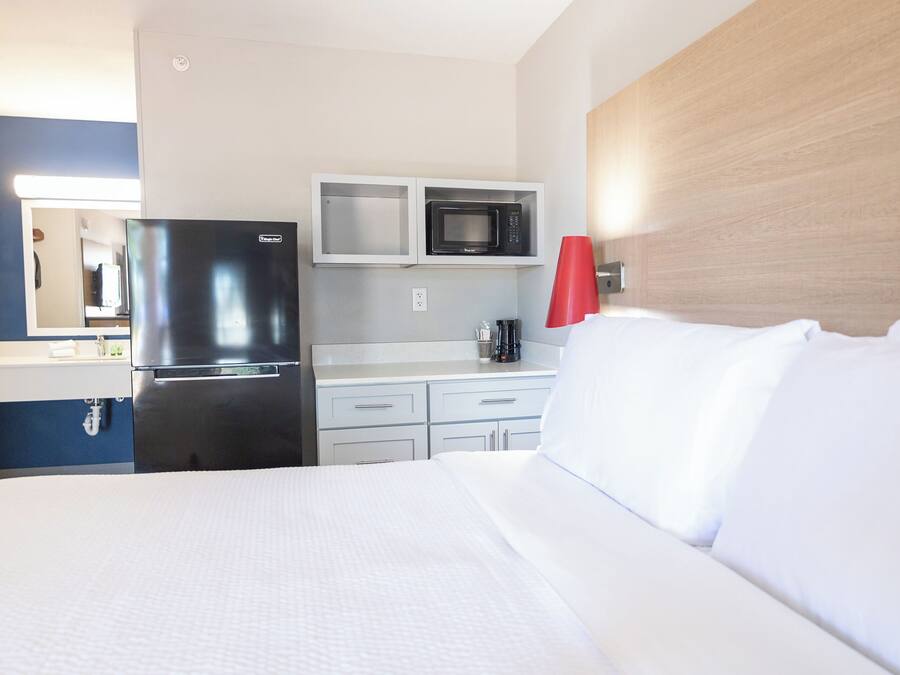 Habitación de hotel con cama, refrigerador, microondas, cafetera y una lámpara roja.
