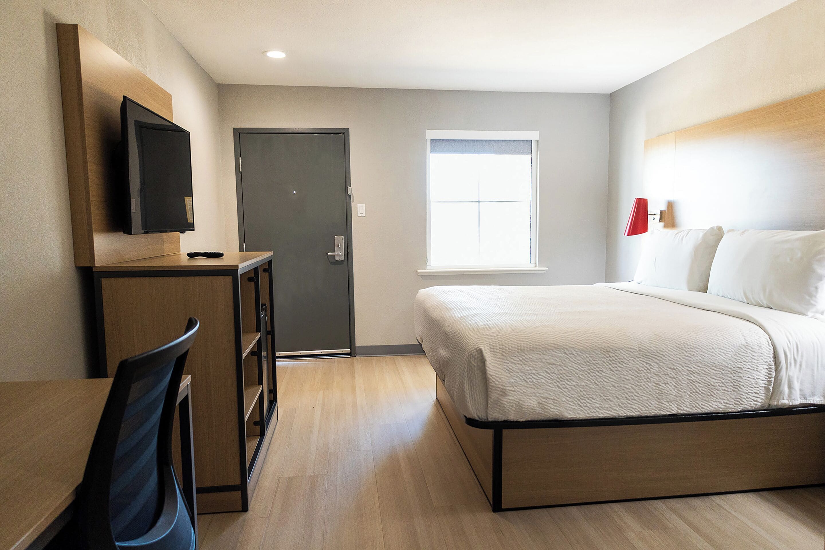 A hotel room with a bed, a desk with a chair, a television, a door, and a window.
