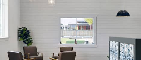 A room with white paneled walls, a large window with a view of a building and a fence, and a potted plant.