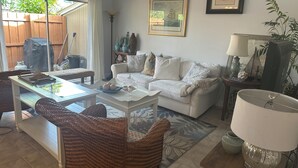 A living room with a white sofa, wicker chairs, a coffee table, and a dining area with a table and chairs. - Hemingway Inspired Villa (Sarasota)